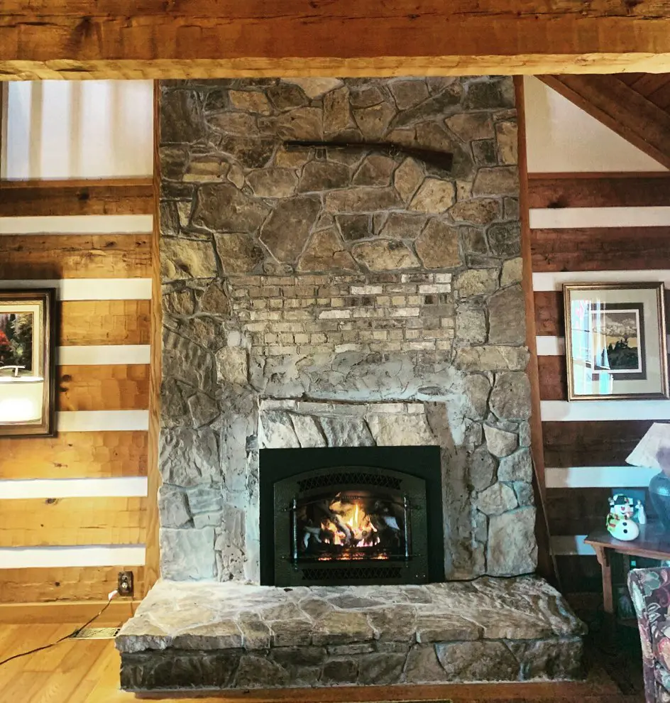 A stone fireplace in the living room of a log cabin.